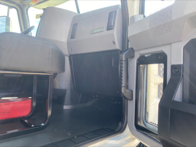 Truck cab interior showing instrument panel area with a green badge labeled 'DE' or 'MACK' unclear, side door opening, and dashboard plastic panels.