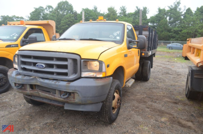 2004 Ford F350 Super Duty rack truck in a yard showing front view with yellow cab and stake-bed equipment.