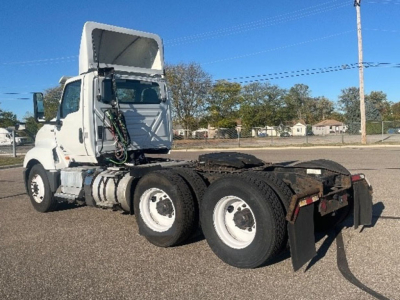 Truck tractor with fifth wheel and dual rear axles visible. Side view shows cab, exposed engine area, and rear mud flaps.