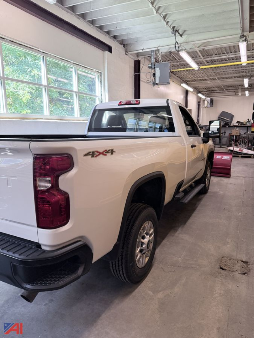Chevrolet Silverado 3500HD pickup truck 4x4 in a workshop with plow hookup visible at rear and crew cab, white paint, 2-door tailgate area, workshop lighting.