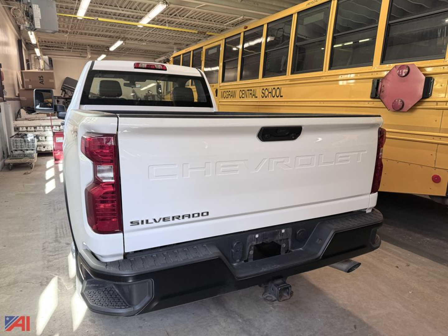 Chevrolet Silverado 3500HD pickup truck rear view in a shop, white body, CHG Vrolet script on tailgate, Silverado badge, hitch, and truck bed in focus
