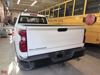 Chevrolet Silverado 3500HD pickup truck rear view in a shop, white body, CHG Vrolet script on tailgate, Silverado badge, hitch, and truck bed in focus