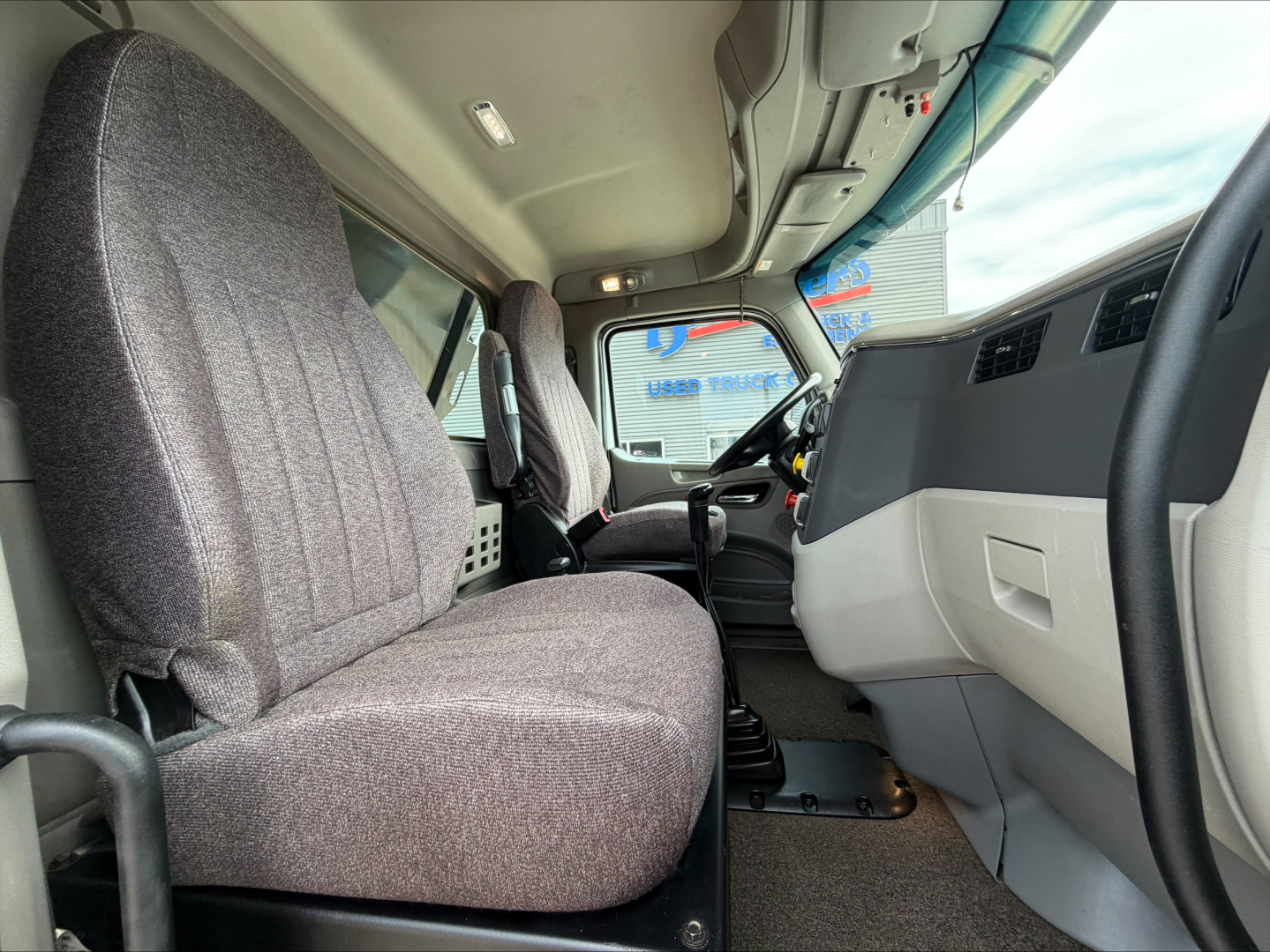 Cab interior of a 2020 Peterbilt 567 dump truck showing grey fabric seats, steering wheel, and dashboard. Visible text includes no legible labels in the photo.
