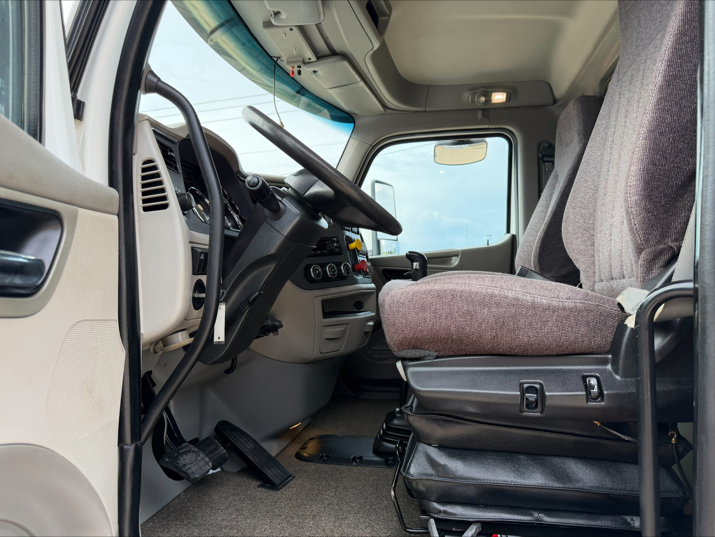 Truck cabin interior showing steering wheel, dashboard, driver seat, and pedals in a Peterbilt cab. Various controls and center console visible.
