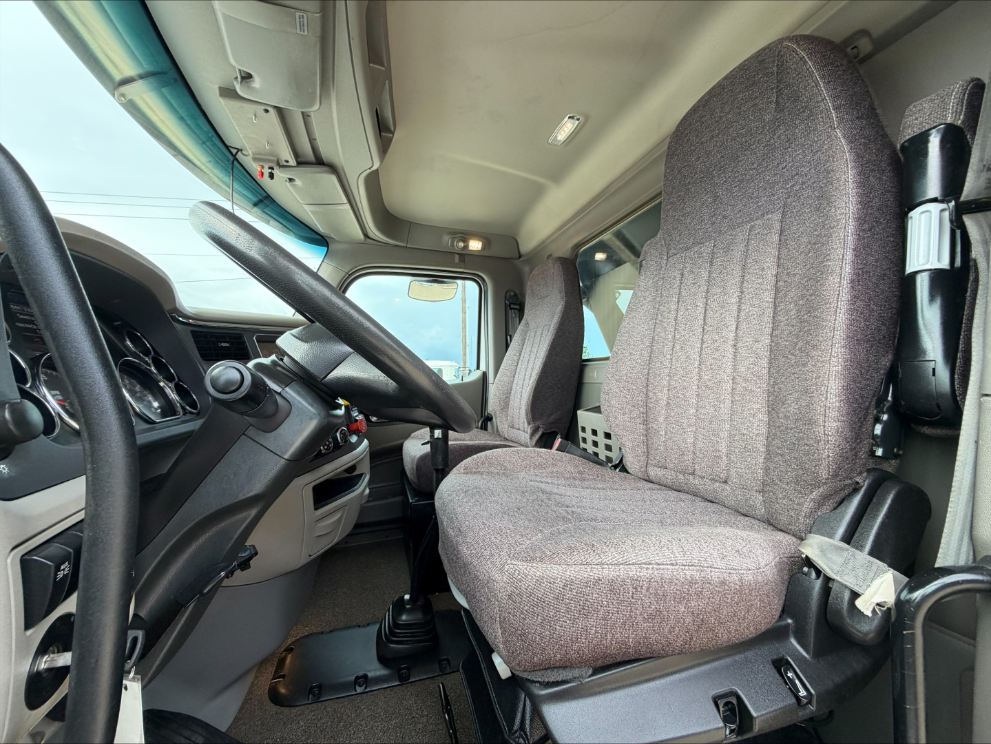 Peterbilt 567 truck cab interior showing driver seat and steering wheel with gray fabric seats and dashboard controls.