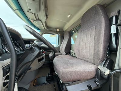 Peterbilt 567 truck cab interior showing driver seat and steering wheel with gray fabric seats and dashboard controls.