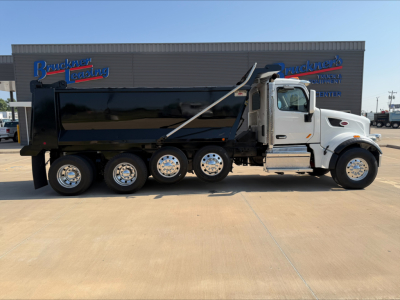 Peterbilt 567 dump truck side view showing black dump body, white cab, chrome wheels, and 'Bedrock' dealership signage in background.