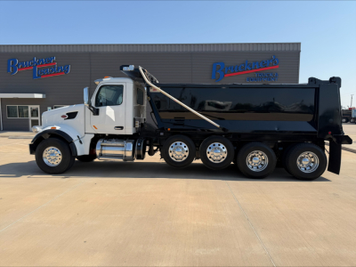 Peterbilt dump truck side profile in front of dealership building with Bracken's Leased? signage; cab white, dump body black, wheels chrome; visible text includes dealership logos on building