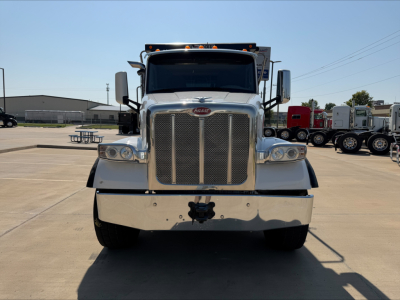 Peterbilt front view of truck with large chrome grille, bumper, and headlights. Emblem on grille. Dump truck in background.