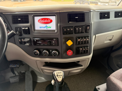 Peterbilt 567 cab interior dashboard with steering wheel, digital display, climate controls, and gear shifter visible.