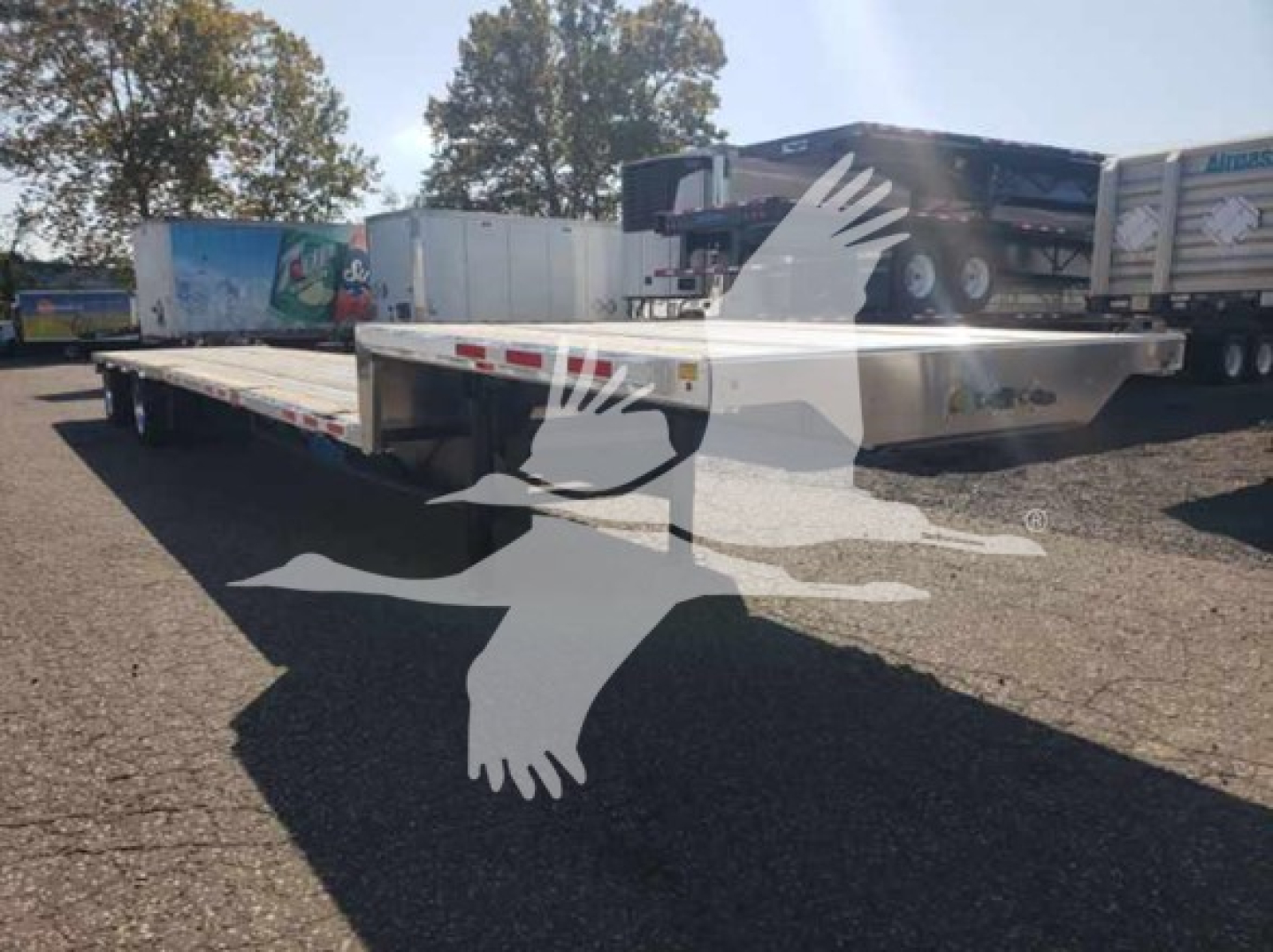 Trailer shown from side view on lot with drop deck, low pro 17.5 model, white with metal surface.