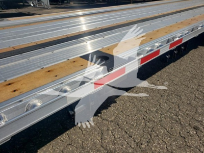 Trailer deck with silver metal beams and wooden planks; side rail with reflective red and white tape; watermark overlay of a handprint graphic.