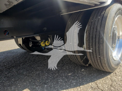 Trailer undercarriage showing suspension and dual tires, with yellow adjustment knobs visible.