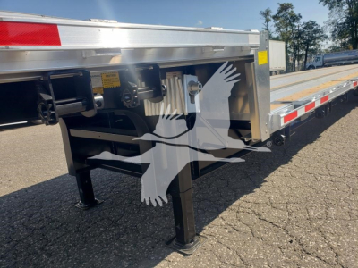 Trailer leg and underside of a drop deck trailer with metal frame, black support legs, and hydraulic components; visible yellow warning label and structural brackets.