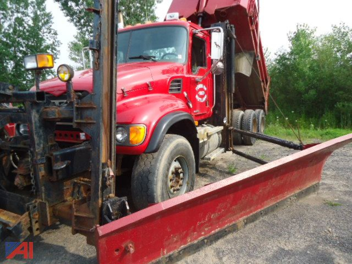 Red Mack Granite CV713 dump truck with plow and wing blades parked on a lot; front cab and blade frame visible.
