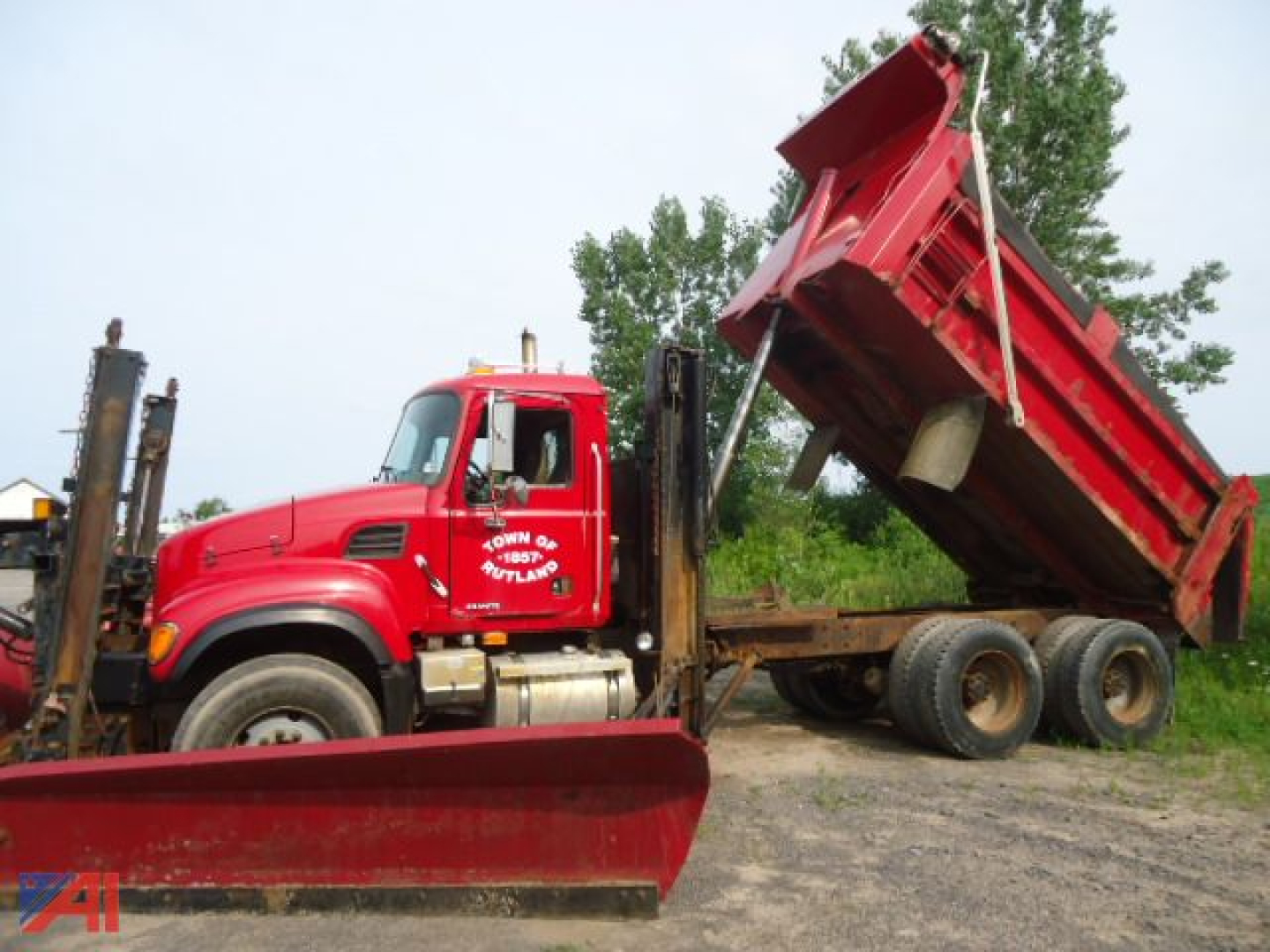 Red Mack Granite CV713 dump truck with plow and wing dumping bed raised, side view showing cab and dual rear axles.