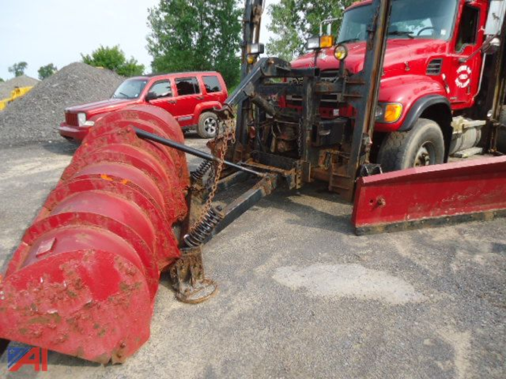 Mack Granite CV713 dump truck with plow and wings showing front snow/ice plow blade and red auger-style snow blower attachment, heavy equipment in a yard.