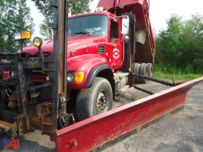 Red Mack Granite CV713 dump truck with plow and wing blades parked on a lot; front cab and blade frame visible.