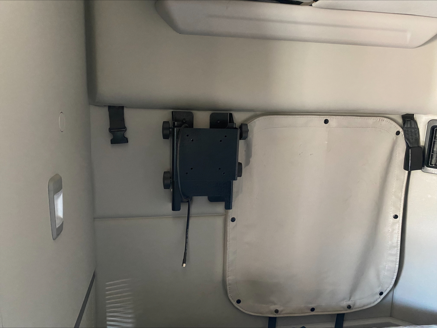 Peterbilt truck cab interior panel with a black rectangular device mounted on the wall and a square light-gray hatch cover next to it.