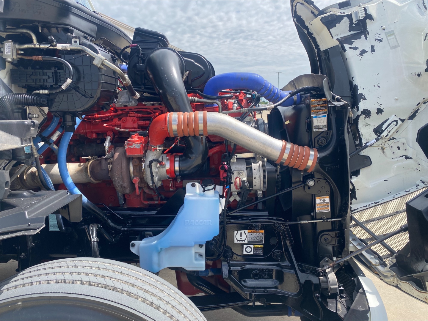 Peterbilt 579 engine bay with red engine, blue hoses, and blue coolant reservoir cap visible; intake manifold and turbo components; side cab exposed.