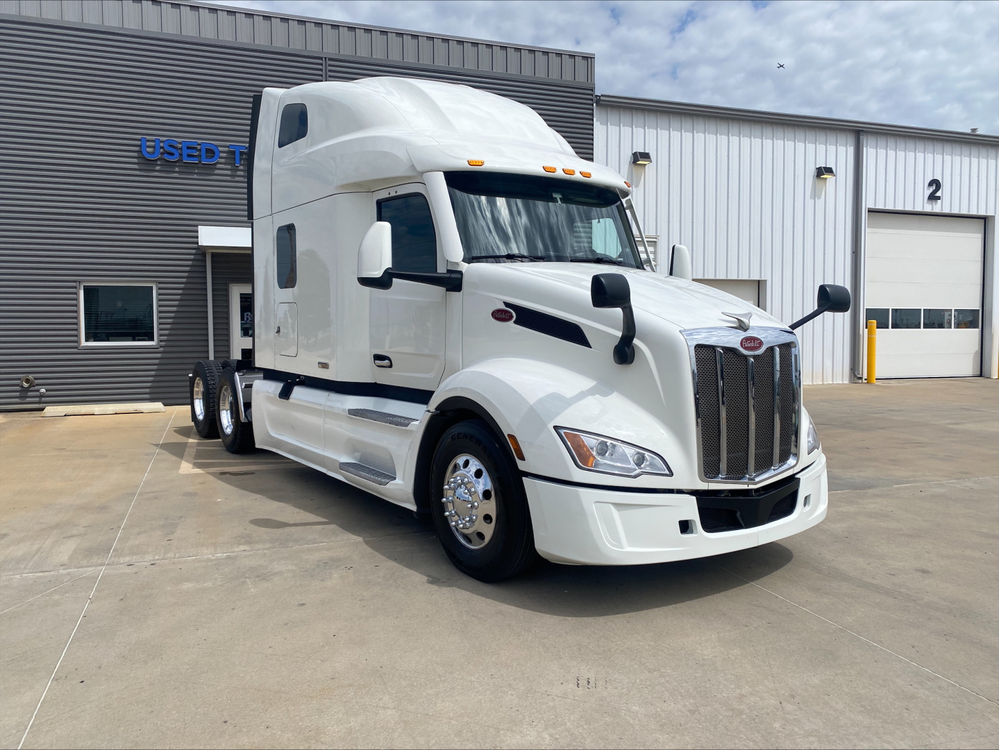 Peterbilt 579 sleeper tractor in white, front-left view, parked outside a service facility.