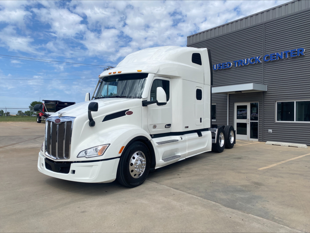 Peterbilt 579 semi-truck in white, parked outside a used truck center, front three-quarter view.