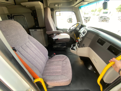 Peterbilt 579 truck cab interior from driver side showing gray fabric seats, steering wheel, dashboard, and yellow interior handle.