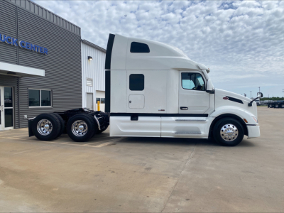 Peterbilt 579 conventional sleeper tractor in white, side view, showing cab with sleeper window and dual rear axles, parked outside dealership.