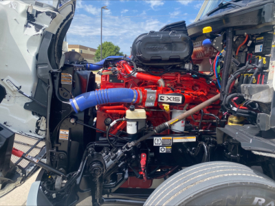 Peterbilt 579 engine bay showing EXi5 red engine with blue intercooler hose, various hoses, wiring, and components inside the cabless front area.