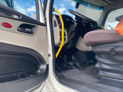 Peterbilt 579 truck interior driver’s seat and open door showing steering column and yellow grab handle.