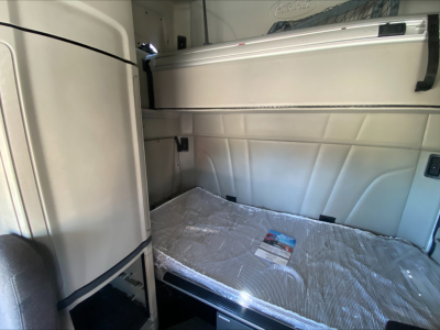 Peterbilt 579 truck interior sleeper area with a folded bunk bed and shiny metallic cover, partial vertical cabinets on left.