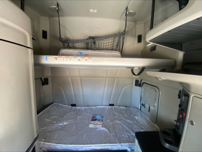 Cab interior of a 2022 Peterbilt 579 sleeper with cargo net, overhead storage, and a bed covered in plastic.