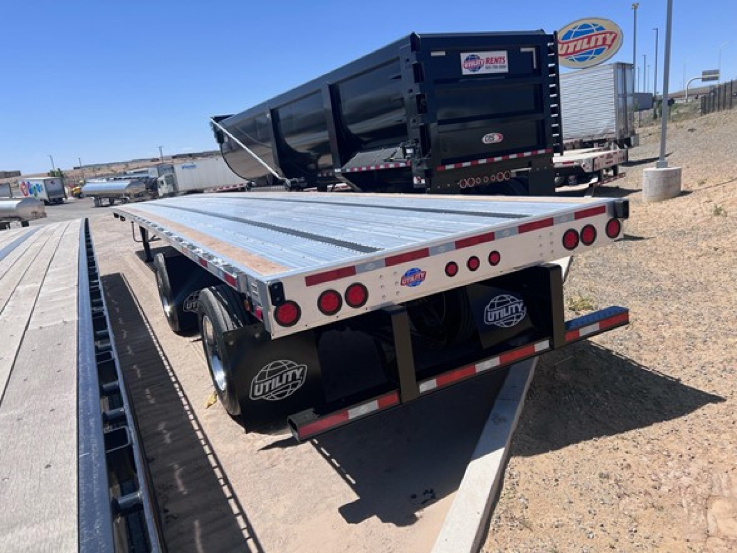 Utility combo flatbed trailer showing a lowered ramp and aluminum deck with rear taillights and Utility logo on spare tires.