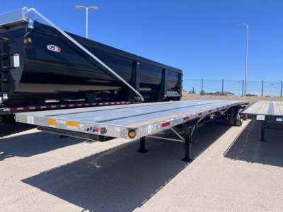 Flatbed trailer in outdoor lot showing long aluminum deck with support legs, safety lights, and side markings; utility combo flatbed with black dump trailer in background.