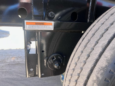 Trailer hitch area showing a Stabilizer/connection pin knob and warning label on a black steel frame beside a tire of a 2025 utility combo flatbed trailer.