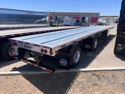 Flatbed trailer with aluminum decking and dual rear axles showing reflective tape and tires.
