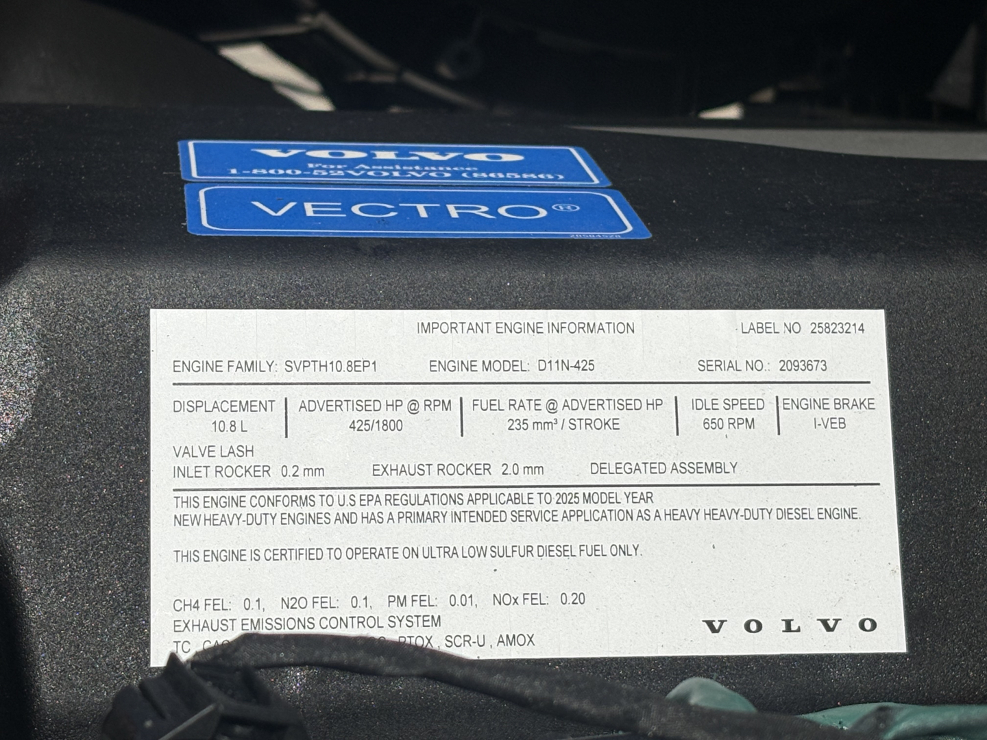 Volvo engine bay showing engine spec label with VIN and engine information plate and blue Volvo/VECTRO stickers.