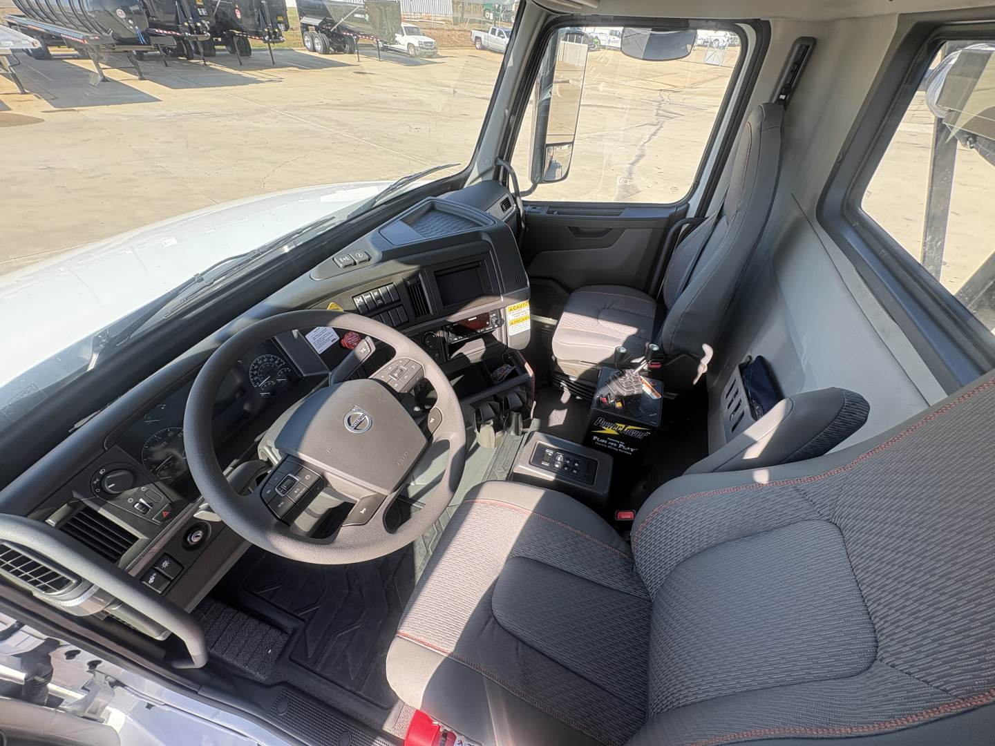  Volvo VHD64B300 truck interior view showing steering wheel, dashboard, driver seat, and passenger seat with center console and control panels.