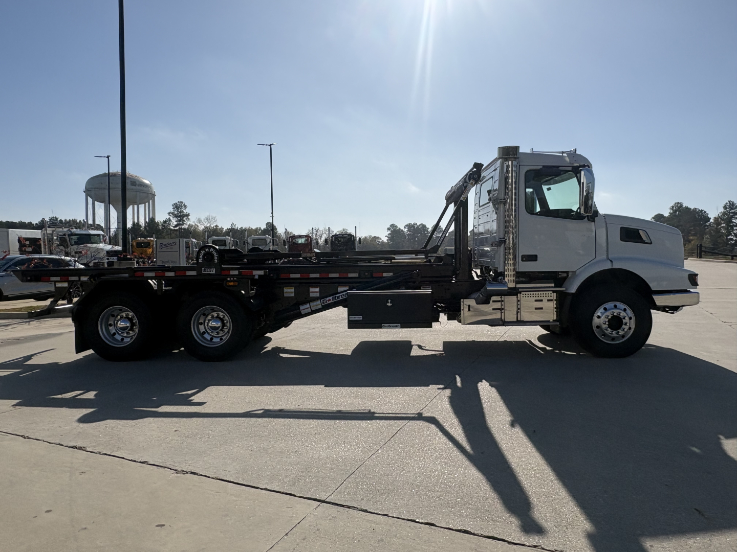 Volvo VHD64B300 roll-off truck in side profile showing cab, long flatbed, winch, and dual rear axles.