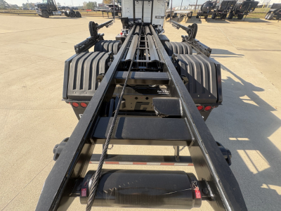 Truck chassis/rail frame of a Volvo VHD64B300 roll-off truck, with heavy steel rails and winch hardware visible along the center, crew cab rear in background.
