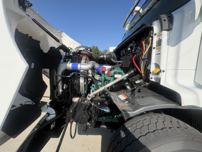 Volvo VHD64B300 engine bay with exposed engine, hoses, wiring, and intercooler piping. Visible labels and components including coolant hoses and battery area.