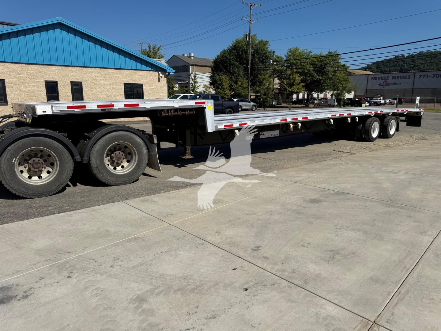 Long flatbed trailer with multi-axle rear section and blue building in background.