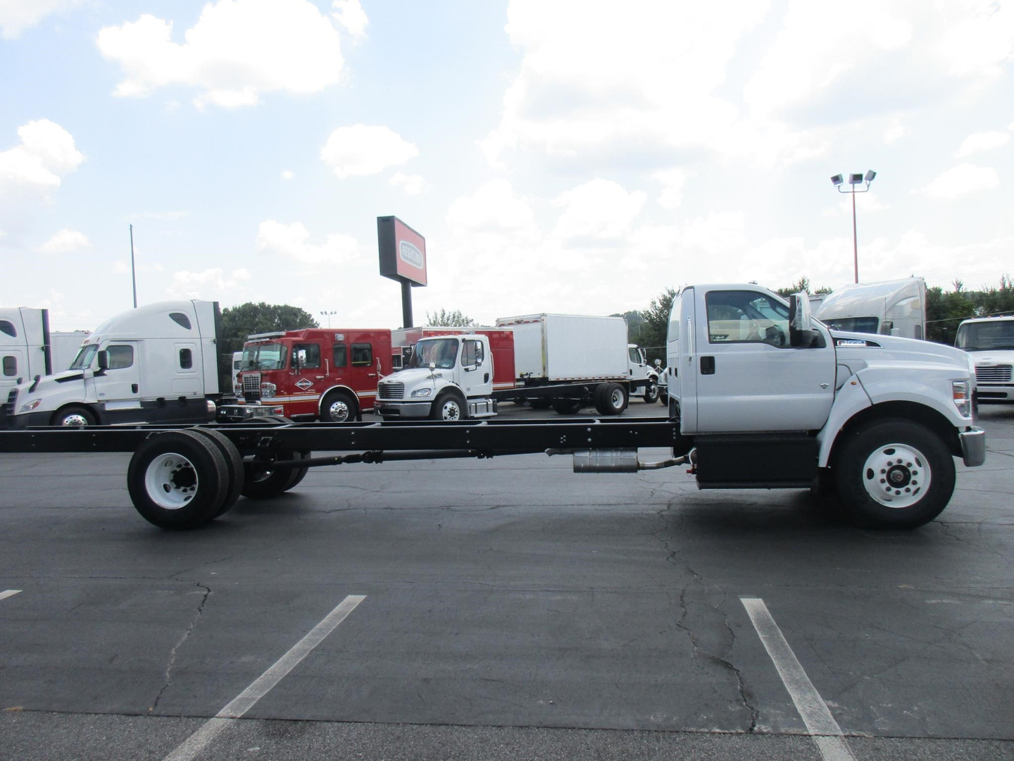 Ford F650 SD cab and chassis truck in a parking lot, side view with empty rear chassis frame and white cab.