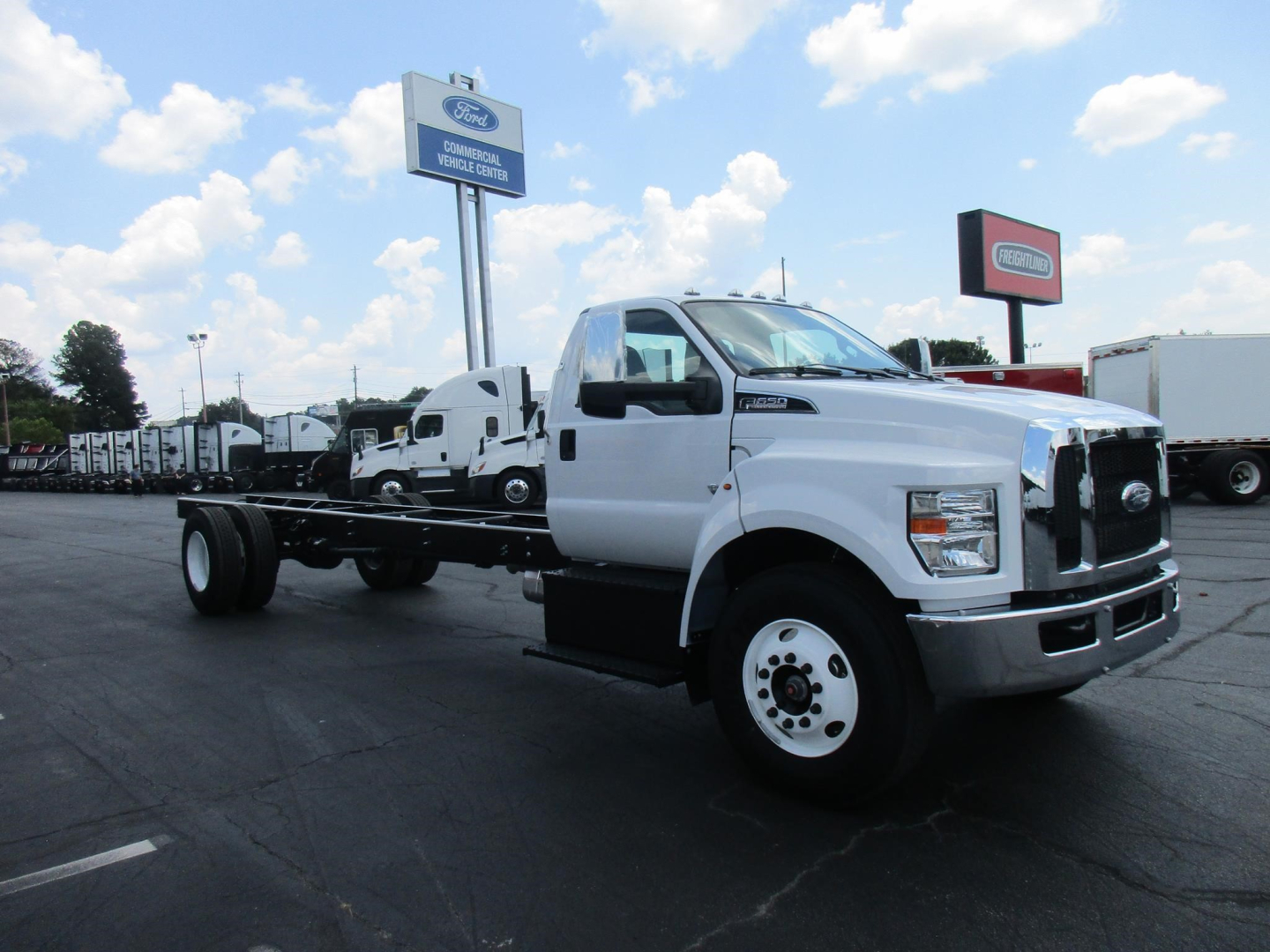 Ford F650 SD cab and chassis truck in a dealership lot showing bare chassis with white cab and front view
