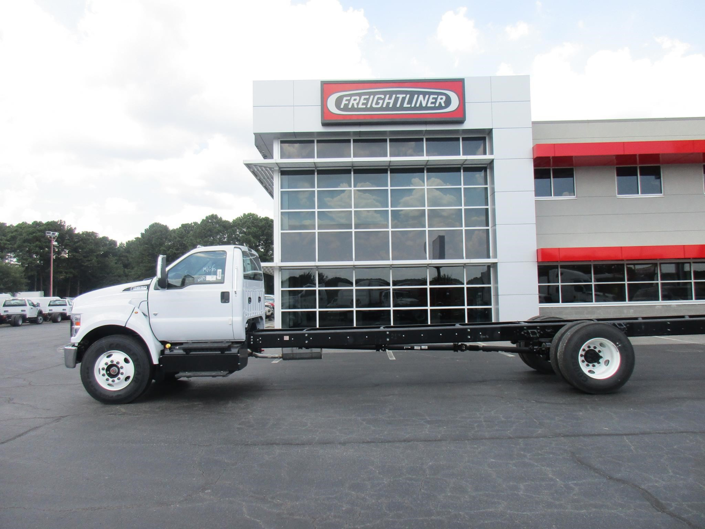 Ford F650 SD cab and chassis truck on lot with Freightliner dealership building in background.