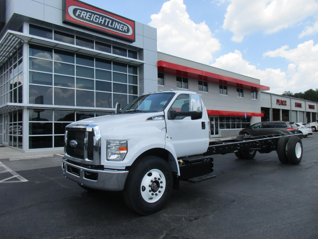 Ford F650 SD cab and chassis truck in front of dealership building, white cab, black chassis, Freightliner signage visible.