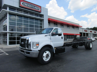Ford F650 SD cab and chassis truck in front of dealership building, white cab, black chassis, Freightliner signage visible.