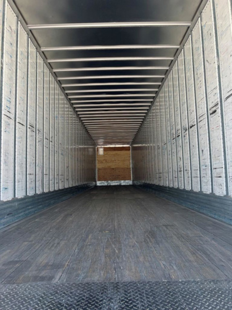 Interior of a utility van trailer showing long empty cargo space with metal side walls and a wooden bulkhead at far end.