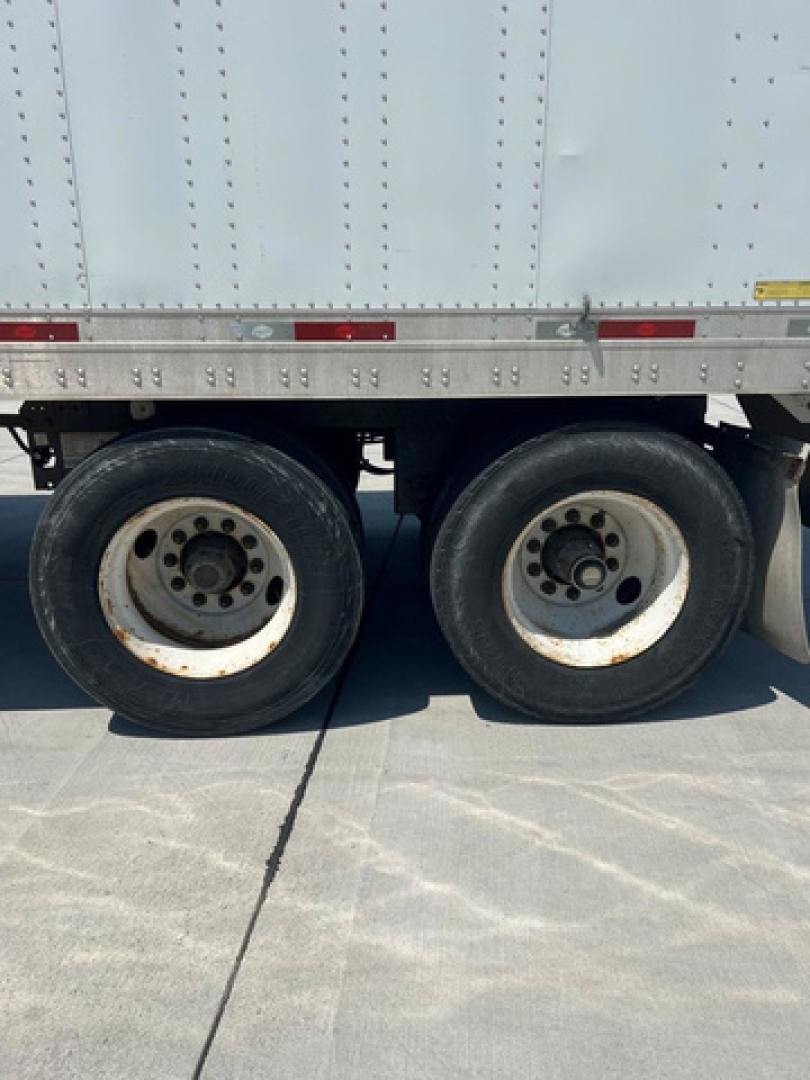 Trailer axle area with two wheels and lower side of cargo trailer; no legible model text visible on image.