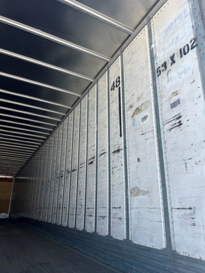 Trailer interior sidewall with metal panels and stamped numbers along the length showing 48 and 53 x 102 on the right; warehouse trailer bay perspective.